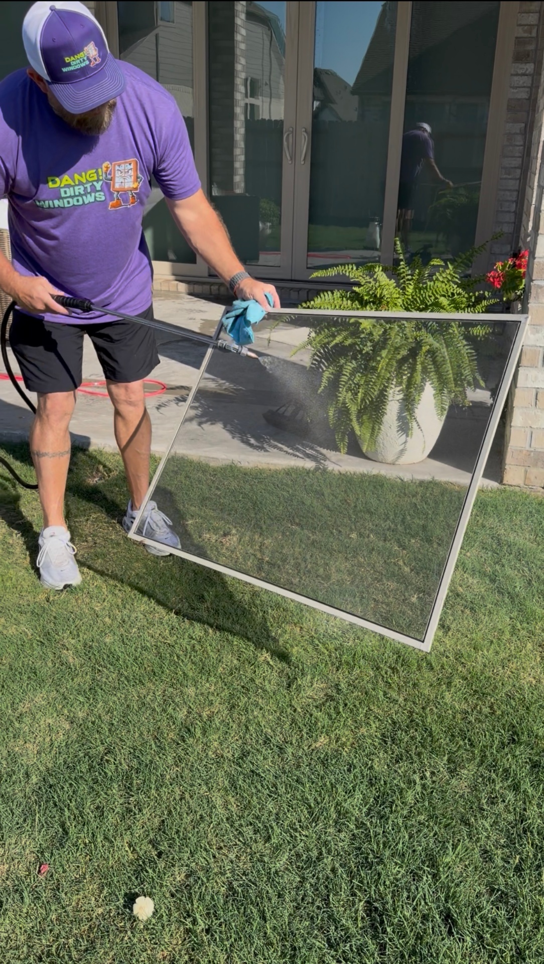 Dang Dirty Windows technician hand-rinsing a window screen on a green lawn in The Woodlands, TX